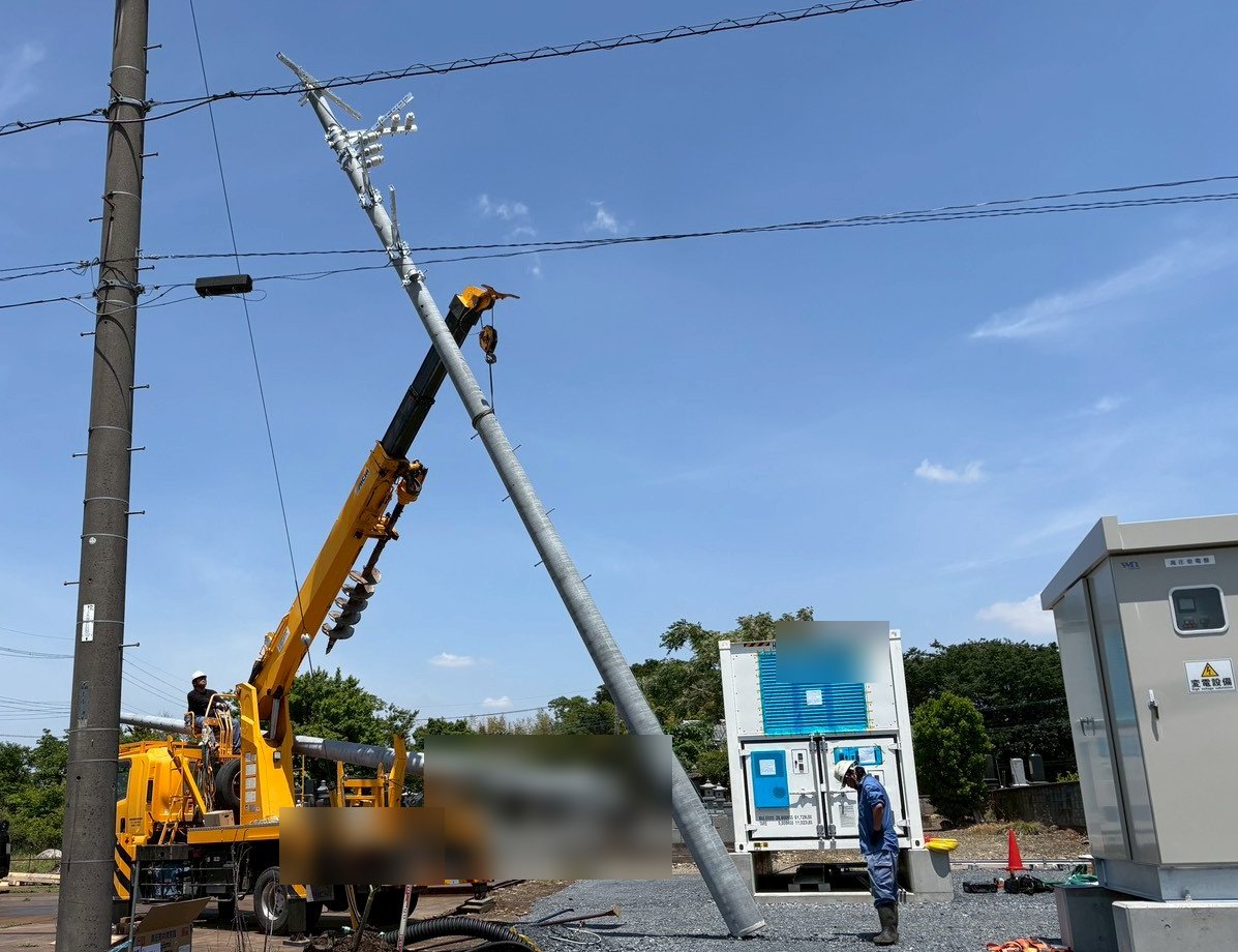 クレーンで鋼管柱を建て起こしている建柱作業